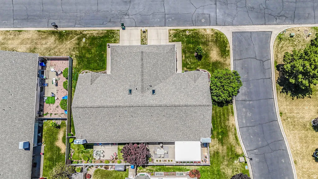 Overhead view of a property featuring a gray shingle roof, a paved driveway, and a concrete patio with a white awning