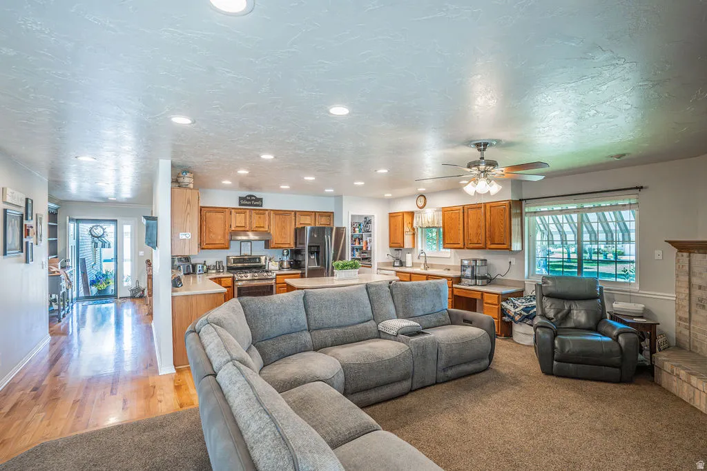 Open-concept living space featuring recessed lighting, a ceiling fan, and a kitchen with wood-finish cabinetry, stainless steel appliances, and an island with bar seating