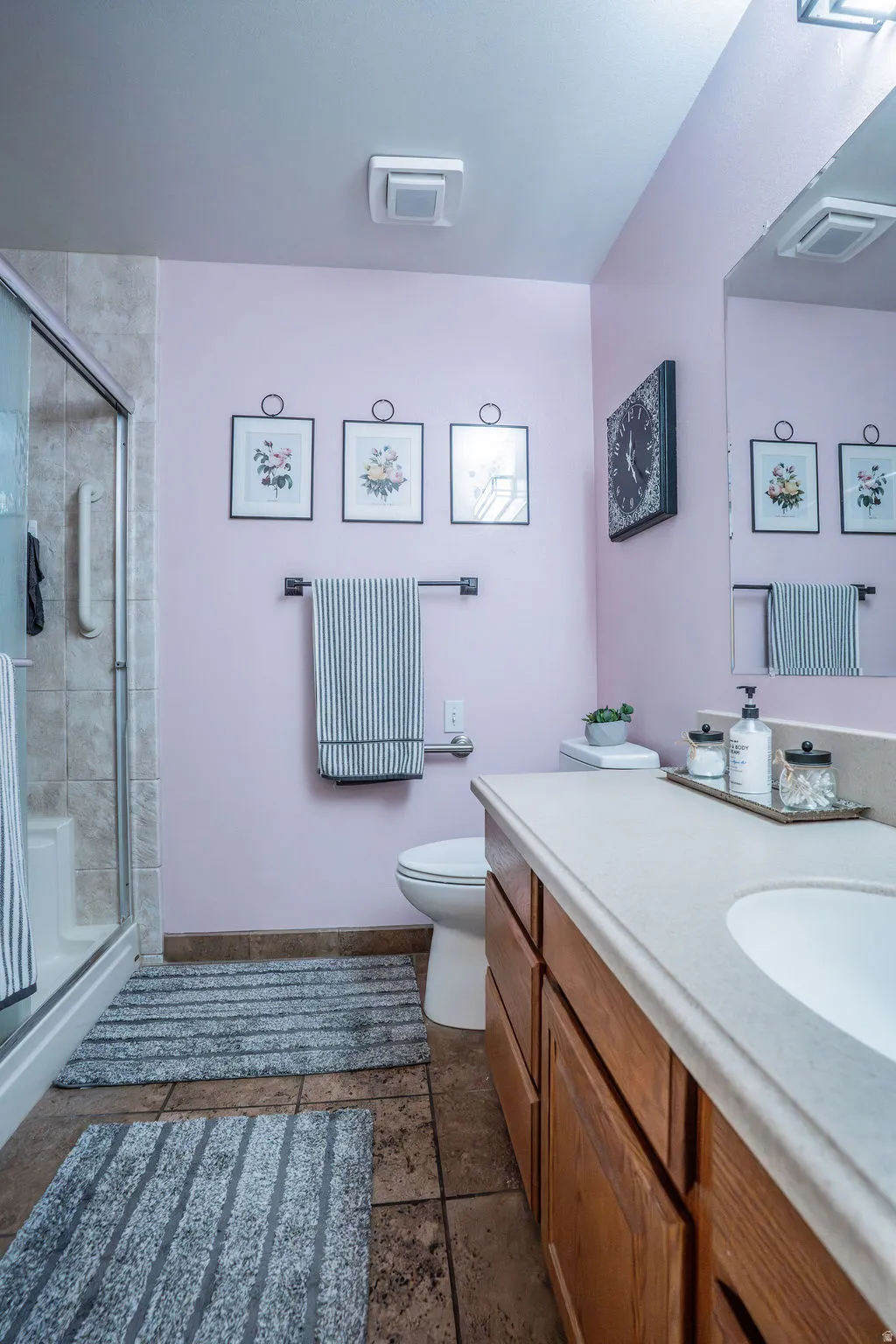 Full bathroom featuring a shower with a clear glass enclosure, a vanity with wood-finish cabinetry, a white countertop with an integrated sink, and large format tile flooring