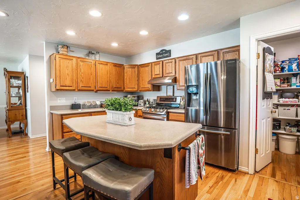 Kitchen featuring wood cabinetry, stainless steel appliances, a center island with countertop seating, recessed lighting, and wood-finish flooring
