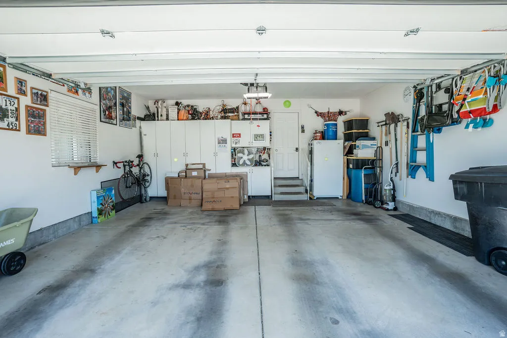 Spacious garage with overhead door, concrete flooring, built-in storage cabinetry, a side window with blinds, and an interior access door