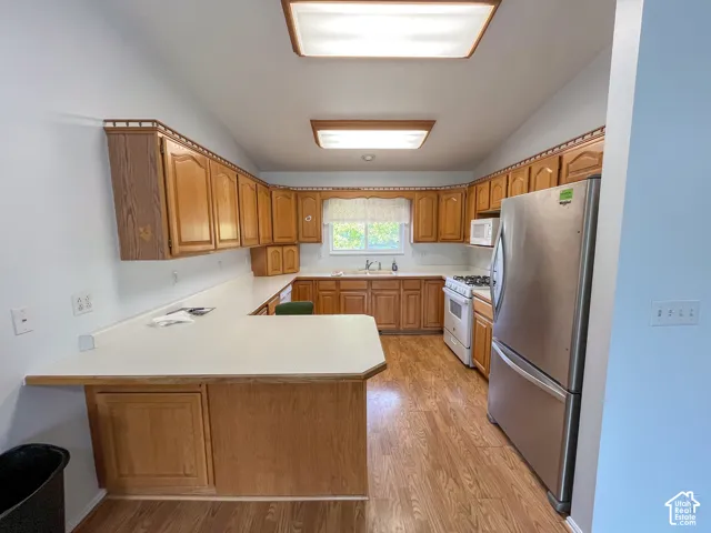 Kitchen featuring wood-finish cabinetry, light countertops, wood-finish flooring, and a stainless steel refrigerator