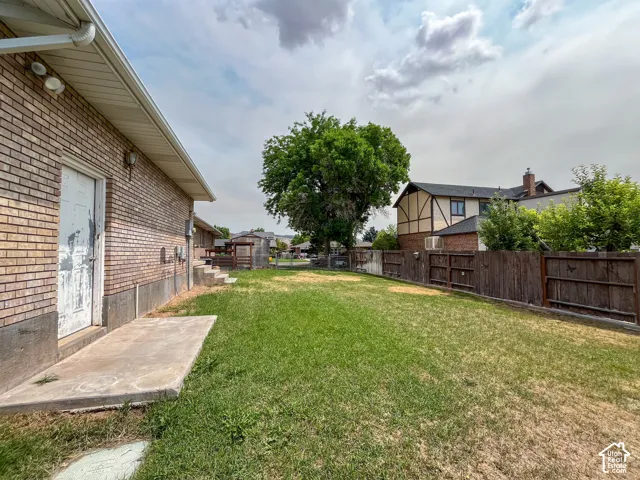 Expansive grassy yard area featuring a mature shade tree and a privacy fence