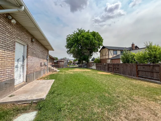 Expansive grassy yard area featuring a mature shade tree and a privacy fence