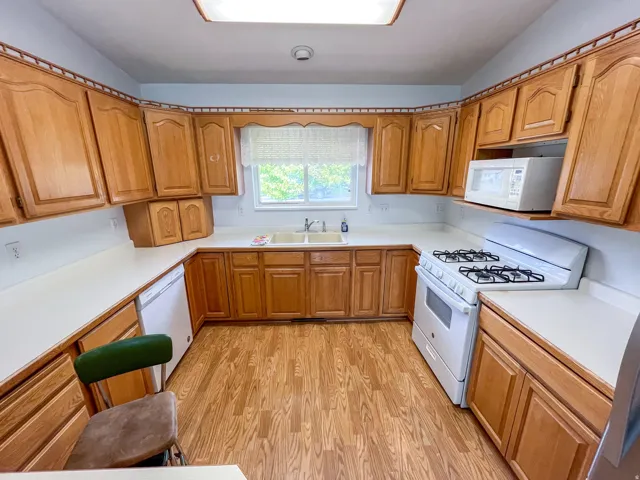 U-shaped kitchen featuring wood cabinetry, white countertops, dual-basin sink, gas range, and wood-finish flooring