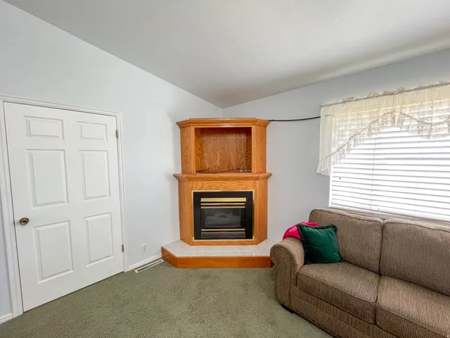 Corner fireplace with light wood-finish mantel and built-in shelving, featuring a tile hearth and a dark metal firebox
