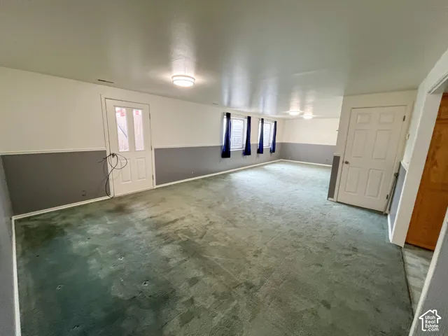 Spacious interior room with light green carpeting, white and gray wainscoting, and multiple windows