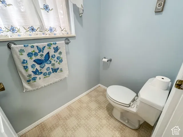 Compact powder room featuring a white toilet, patterned vinyl flooring, light blue walls, and a window with a sheer curtain