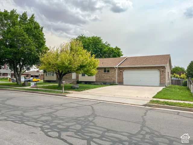 Brick exterior featuring a two-car garage with a white door, concrete driveway, and mature landscaping
