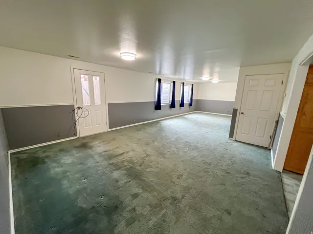 Spacious interior room with light green carpeting, white and gray wainscoting, and multiple windows