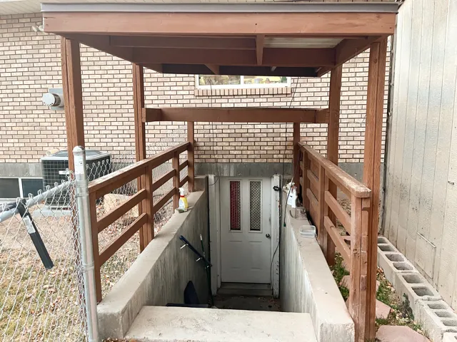 Covered exterior entrance featuring wooden railings and steps leading to a white door with vertical glass panels
