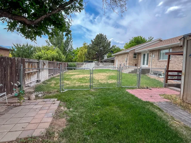Expansive backyard featuring a partial chain-link fence, a secondary wooden privacy fence, a brick patio area, and a large lawn space