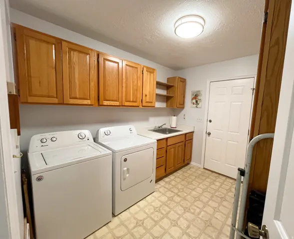 Laundry area featuring extensive wood cabinetry, a utility sink, a light fixture, and patterned flooring