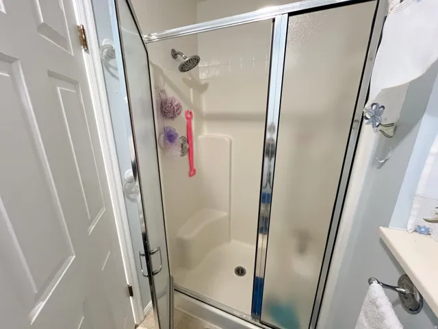 Enclosed shower stall with a built-in seat, a chrome showerhead, and sliding frosted glass doors