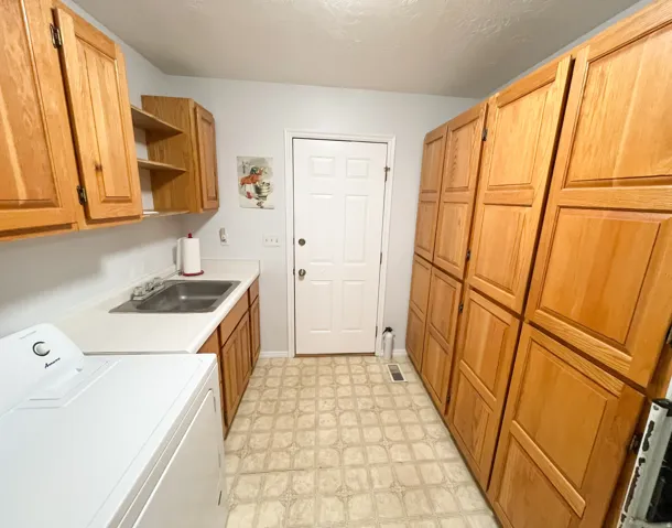 Utility room featuring extensive wood-finish cabinetry, a utility sink, and white countertops
