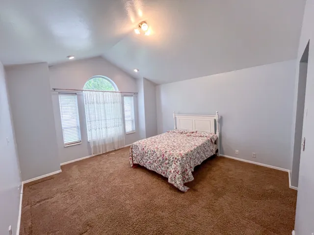 Vaulted ceiling room featuring an arched window, two rectangular windows with blinds, recessed lighting, and a neutral wall color