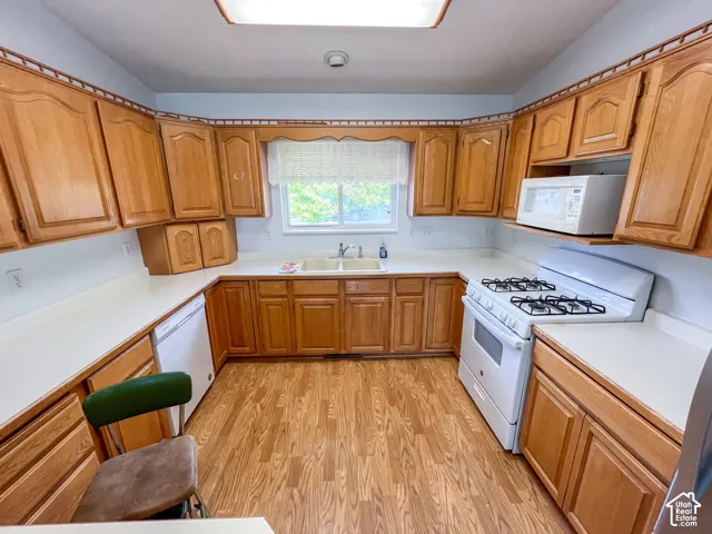 U-shaped kitchen featuring wood cabinetry, white countertops, dual-basin sink, gas range, and wood-finish flooring