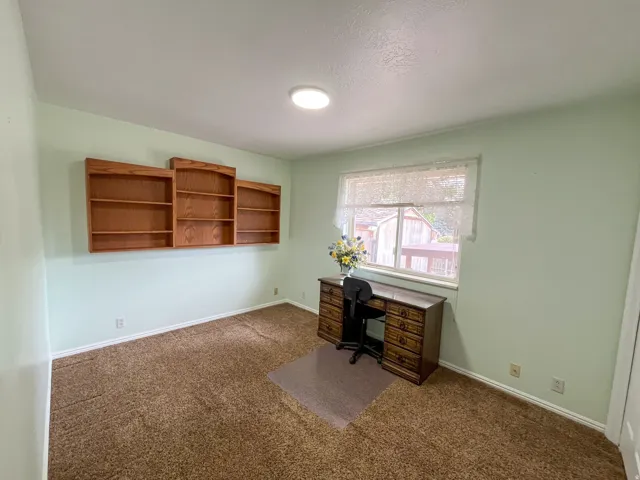 Room featuring light green walls, brown carpeting, and a window with white lace curtains
