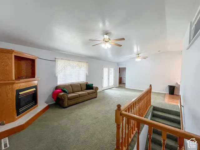 Spacious living area featuring a built-in fireplace with a wood surround, large window with blinds, dual ceiling fans, and double French doors