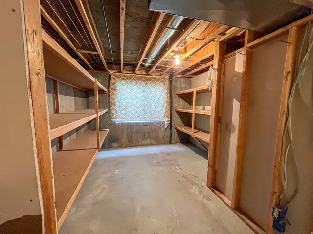 Basement storage area featuring extensive built-in wooden shelving, concrete flooring, and exposed ceiling joists