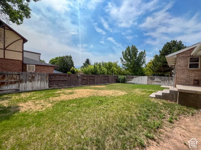 Spacious backyard featuring a large grass area, wood fencing, and mature trees