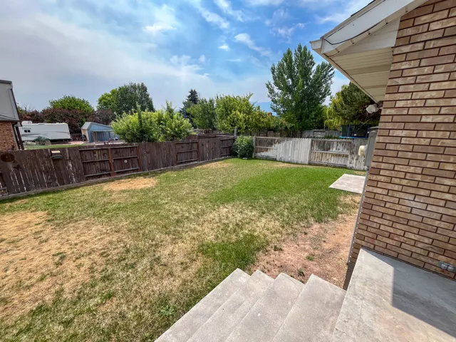 Spacious backyard featuring a combination of wood and white privacy fencing, mature trees along the perimeter, and a concrete patio space