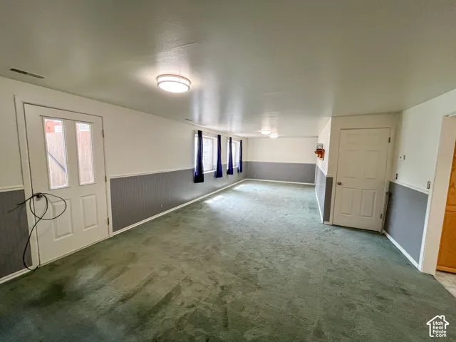 Spacious room featuring green carpeting, white and gray wainscoting, and multiple windows