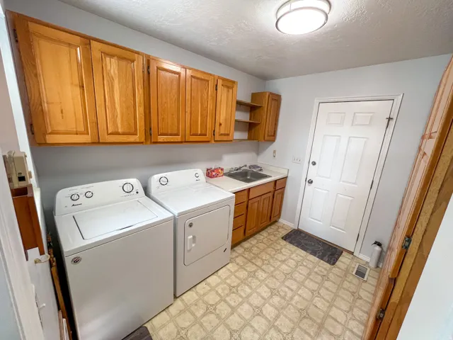 Utility room featuring wood-finish cabinetry, a sink with a countertop, and patterned vinyl flooring
