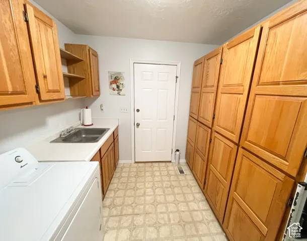 Utility room featuring extensive wood-finish cabinetry, a utility sink, and white countertops