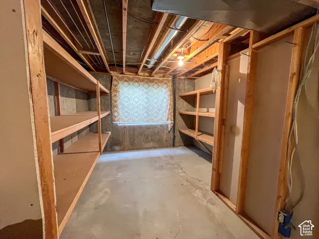 Basement storage area featuring extensive built-in wooden shelving, concrete flooring, and exposed ceiling joists