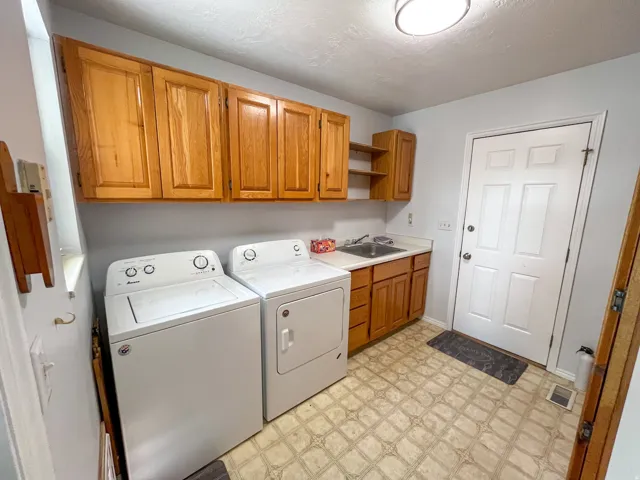 Utility room featuring light wood cabinetry, a utility sink with a white countertop, and patterned vinyl flooring