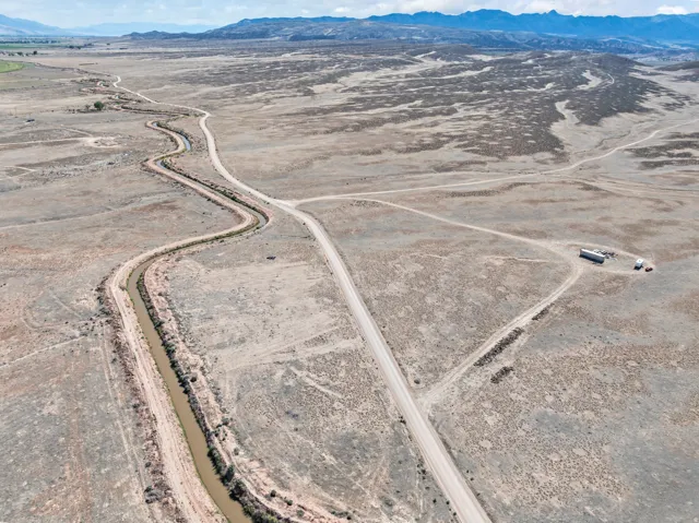 Expansive aerial landscape featuring a winding waterway, unpaved roads, and distant mountainous terrain