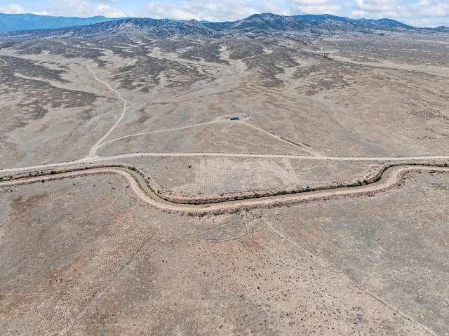Expansive arid landscape featuring a winding waterway, distant mountains, and multiple unpaved roads