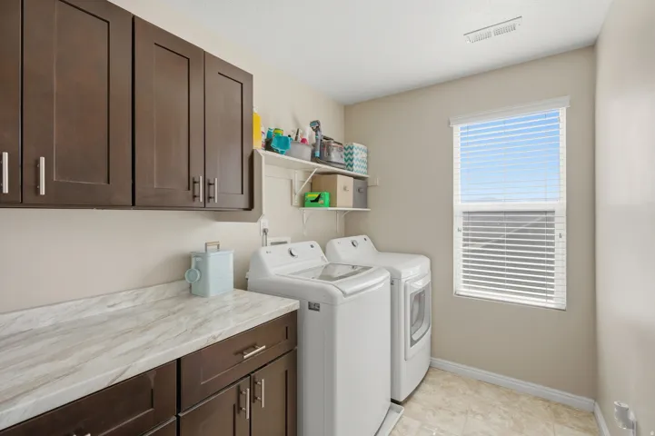 Laundry area featuring dark wood-finish cabinetry, a patterned countertop, and a window with blinds