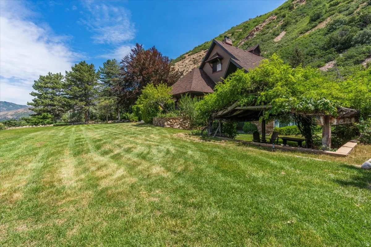 Expansive landscaped lawn with a covered pergola feature, mature trees, and natural mountain backdrop