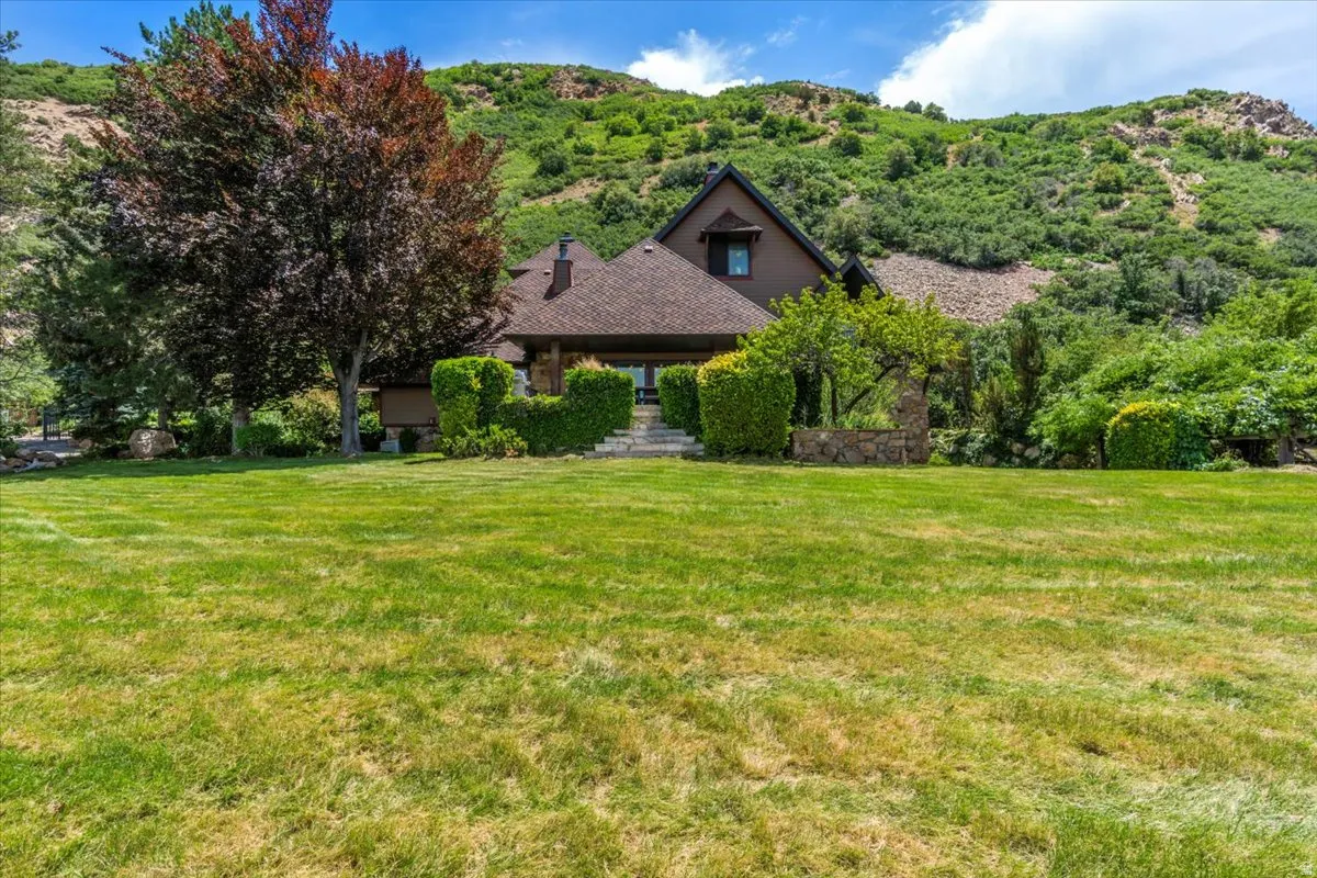 Expansive front lawn with a backdrop of a sloped, tree-covered hillside