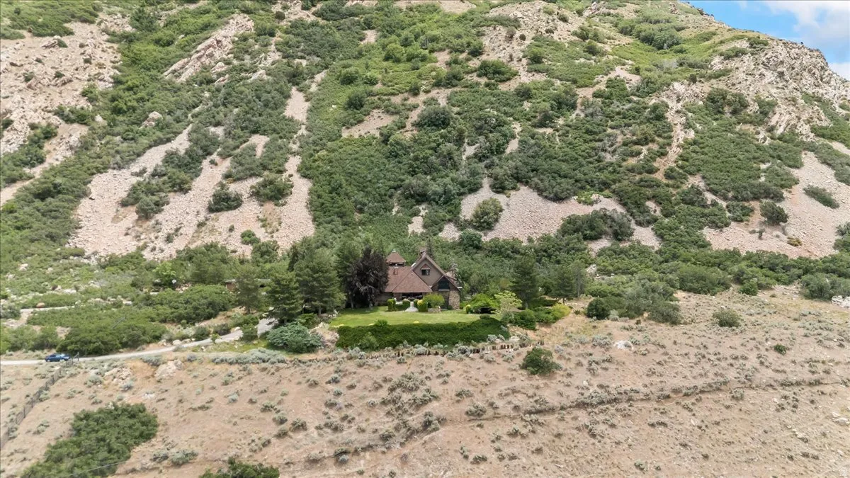 Stone exterior dwelling with a conical roof nestled into a mountainside with varied vegetation, featuring a manicured lawn and mature trees