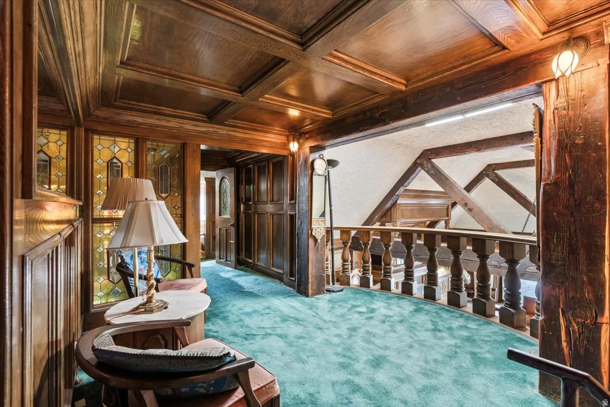 Wood-paneled hallway featuring a coffered ceiling and ornate balustrade overlooking architectural beams