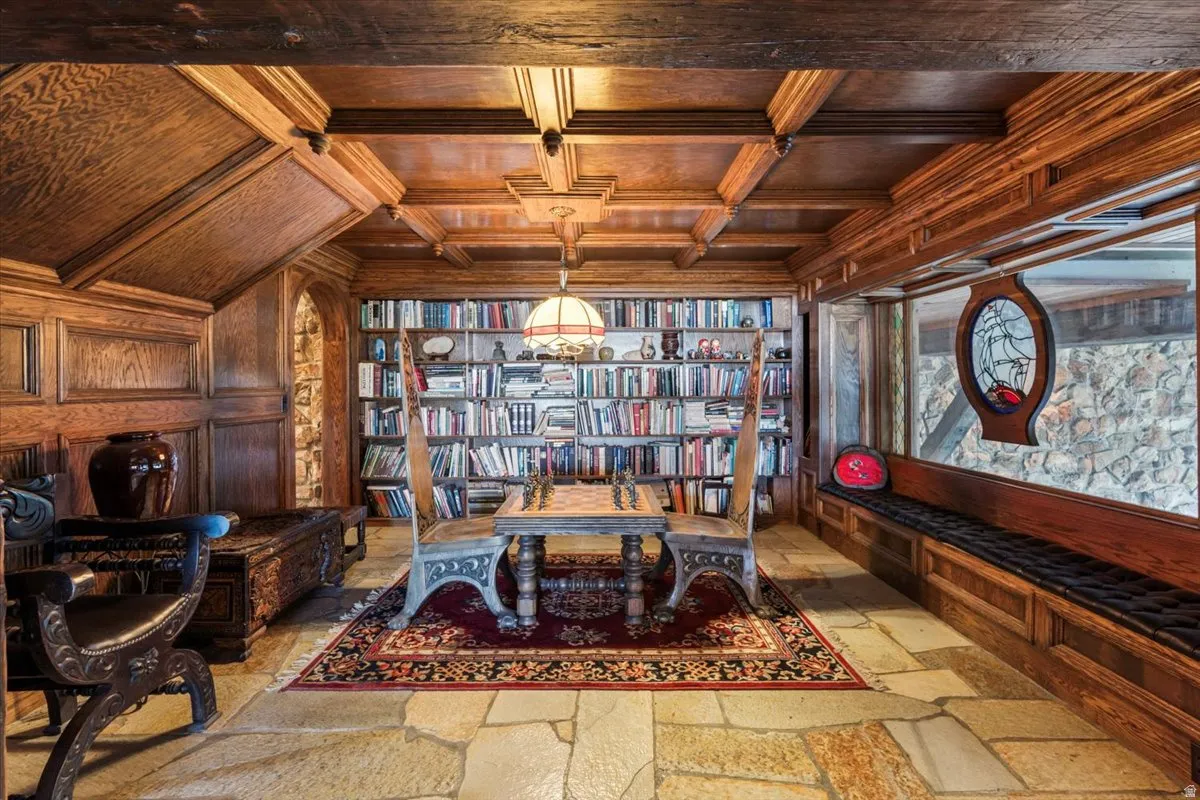 Room featuring stone flooring, a built-in window bench with a dark cushion, extensive wood paneling, wood-beamed ceilings, and a built-in bookshelf