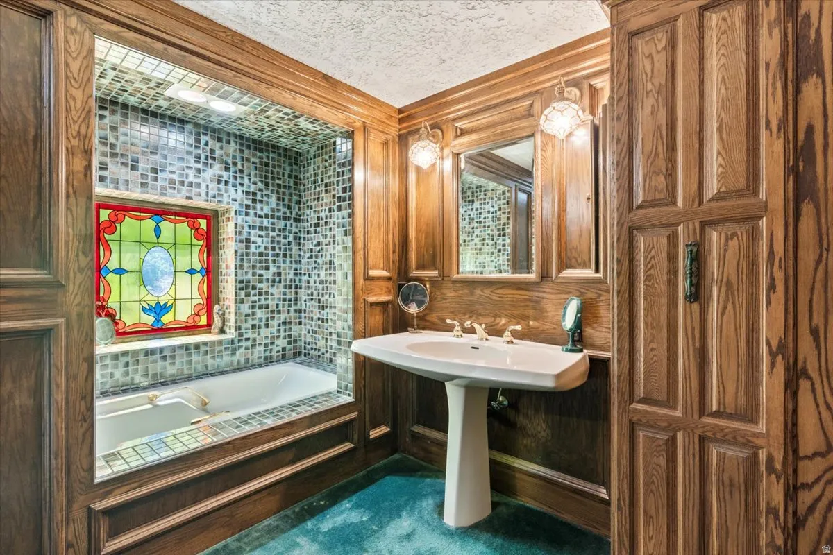 Bathroom featuring a built-in bathtub with mosaic tile surround, a stained glass window, wood paneling, a pedestal sink, and built-in cabinetry