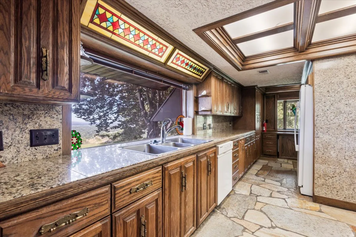 Kitchen featuring wood cabinetry, stone countertops, a double basin sink, and flagstone flooring
