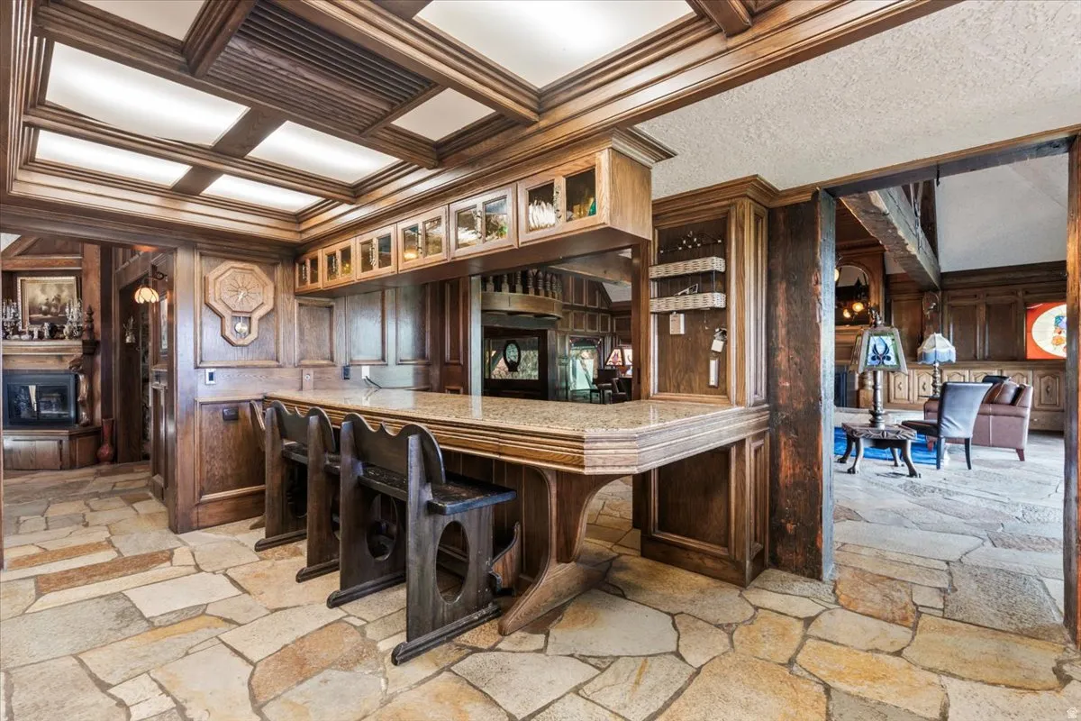 Custom bar area featuring wood paneling, built-in cabinetry with glass fronts, and a stone countertop