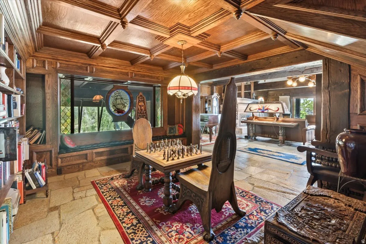 Spacious room featuring extensive wood coffered ceilings, stone tile flooring, built-in shelving, a window seat, and a decorative stained glass insert