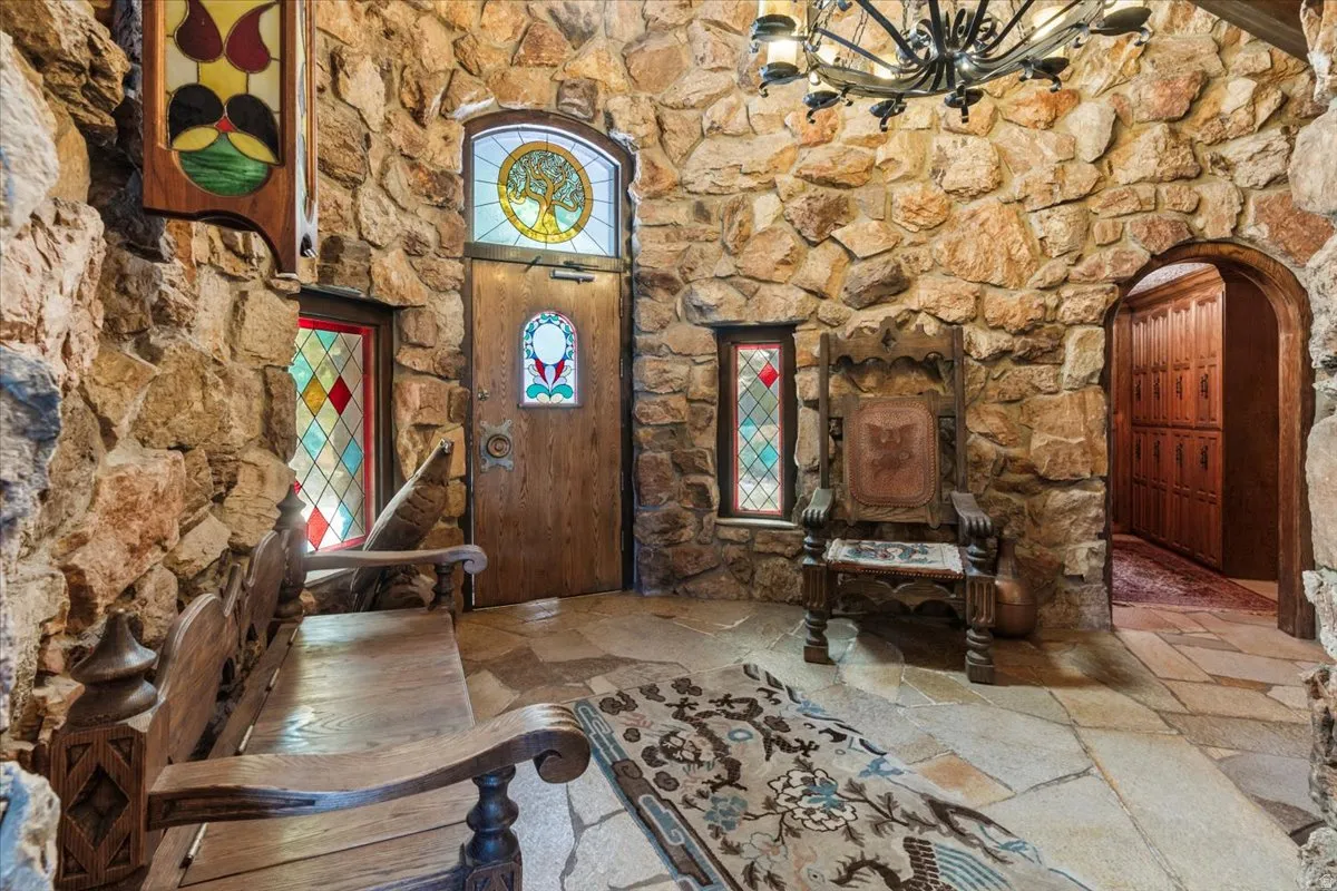 Stone-clad entryway featuring flagstone flooring, a wooden entry door with stained glass, additional stained glass windows, and a wrought iron chandelier