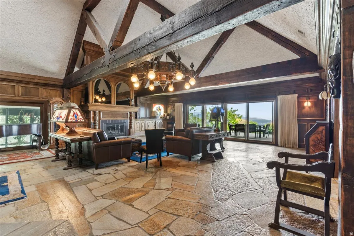 Expansive living area featuring flagstone flooring, exposed wood beams, a prominent fireplace with a detailed wood mantel, and large sliding glass doors opening to an exterior space