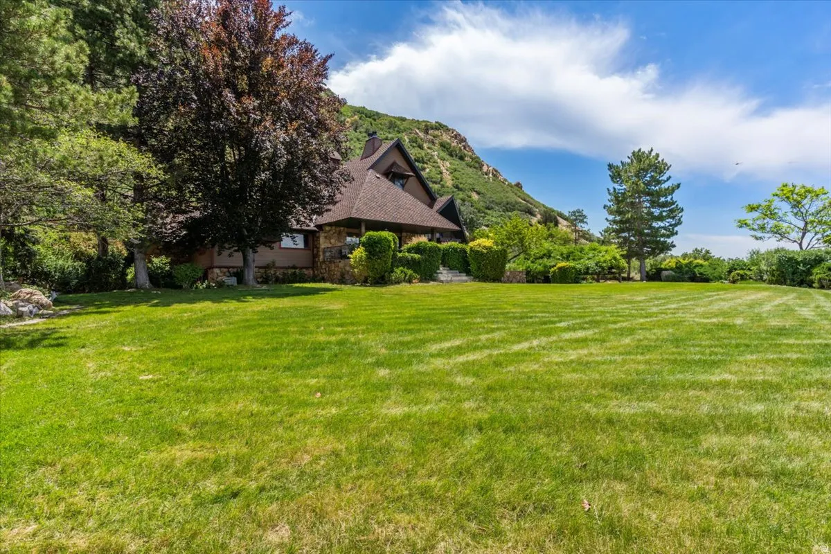 Expansive green lawn with mature trees and a traditional-style home featuring a stone facade and shingle roof