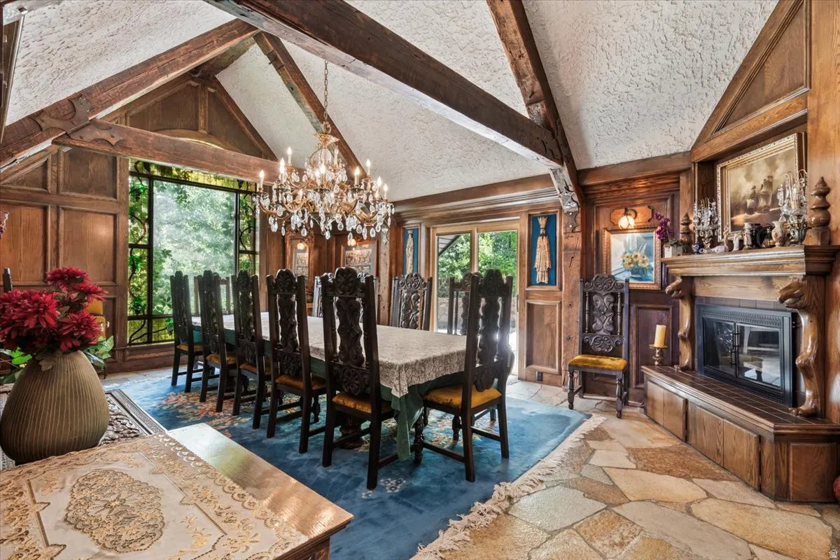 Vaulted ceiling with exposed wood beams, floor-to-ceiling windows, wood paneled walls, a built-in fireplace, and flagstone flooring