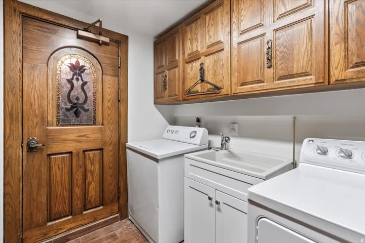 Laundry area featuring wood-finish flooring, a utility sink with a base cabinet, and overhead wood cabinetry