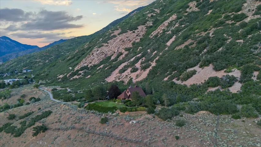 Mountain-side residence featuring a brown roof and a green lawn, surrounded by natural vegetation and rock formations