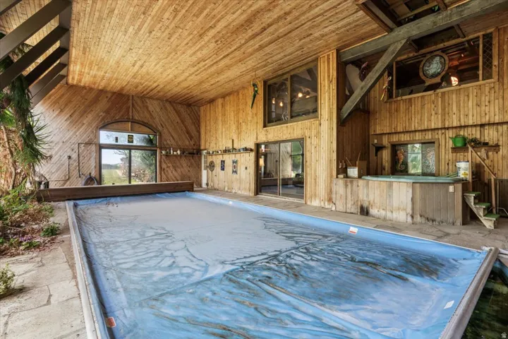 Indoor swimming pool enclosure featuring extensive wood paneling, wood-finish ceiling, and exposed structural beams